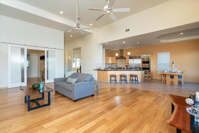 living room with light hardwood / wood-style floors, a barn door, ceiling fan, and a high ceiling