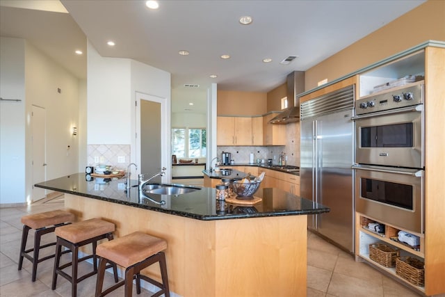 kitchen featuring light brown cabinetry, sink, light tile patterned floors, appliances with stainless steel finishes, and wall chimney range hood