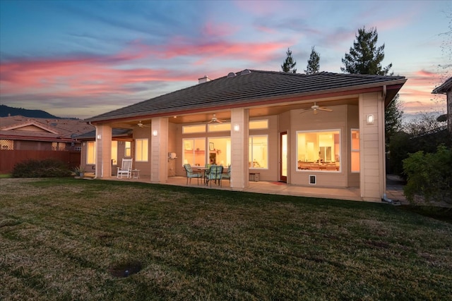 back house at dusk featuring a patio, ceiling fan, and a lawn