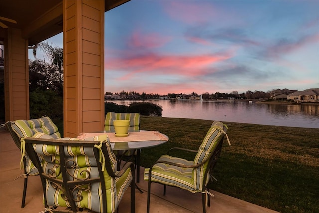 patio terrace at dusk with a water view and a yard