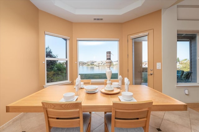 tiled dining space with a water view and a tray ceiling