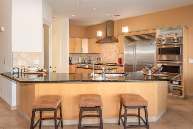 kitchen with sink, a kitchen bar, kitchen peninsula, stainless steel appliances, and wall chimney exhaust hood