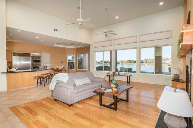 tiled living room featuring a high ceiling, ceiling fan, a healthy amount of sunlight, and a water view