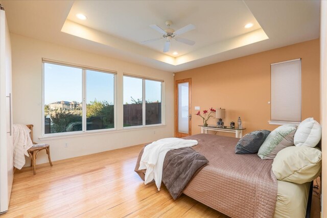 bedroom with light wood-type flooring, ceiling fan, and a tray ceiling