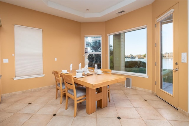 tiled dining space with a tray ceiling and a water view