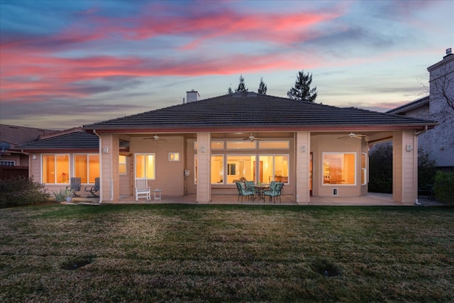 back house at dusk featuring a yard, a patio area, and ceiling fan