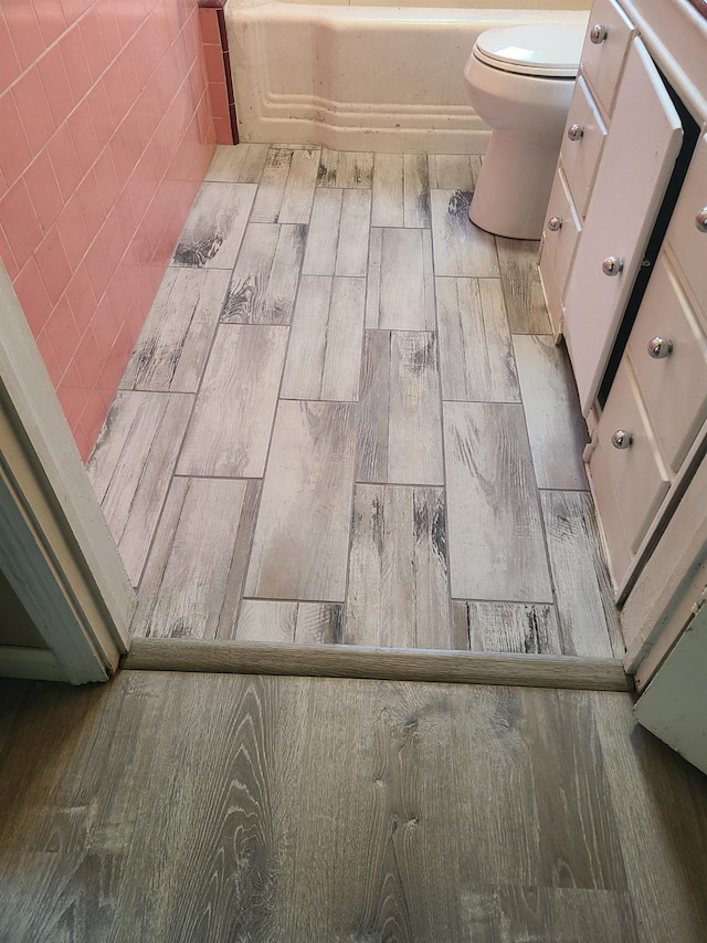 bathroom with toilet, a bath, and hardwood / wood-style floors