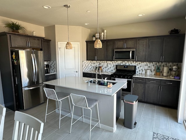 kitchen featuring hanging light fixtures, stainless steel appliances, decorative backsplash, a kitchen island with sink, and sink