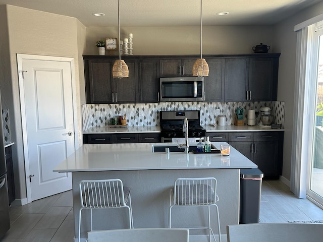 kitchen with pendant lighting, a center island with sink, decorative backsplash, appliances with stainless steel finishes, and sink