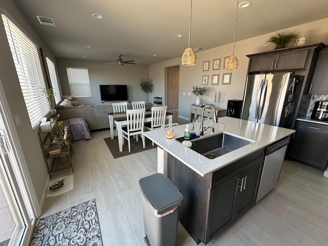 kitchen featuring pendant lighting, sink, stainless steel appliances, a center island with sink, and dark brown cabinetry