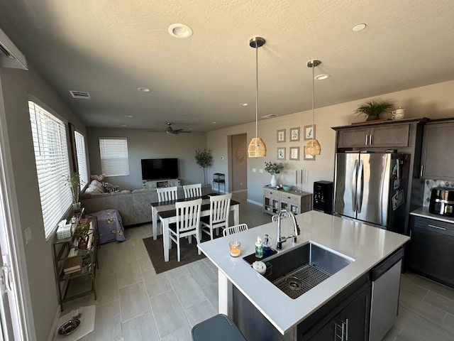 kitchen featuring a kitchen island with sink, stainless steel appliances, hanging light fixtures, ceiling fan, and sink