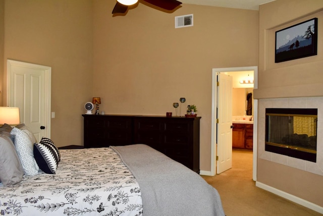 bedroom featuring ceiling fan, a tile fireplace, ensuite bath, and carpet flooring