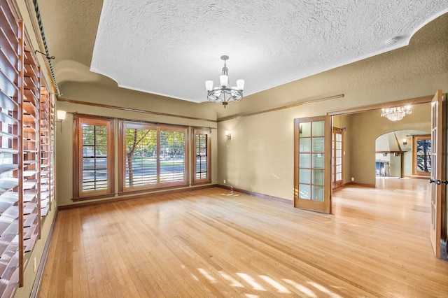 unfurnished room featuring a textured ceiling, an inviting chandelier, and light hardwood / wood-style floors