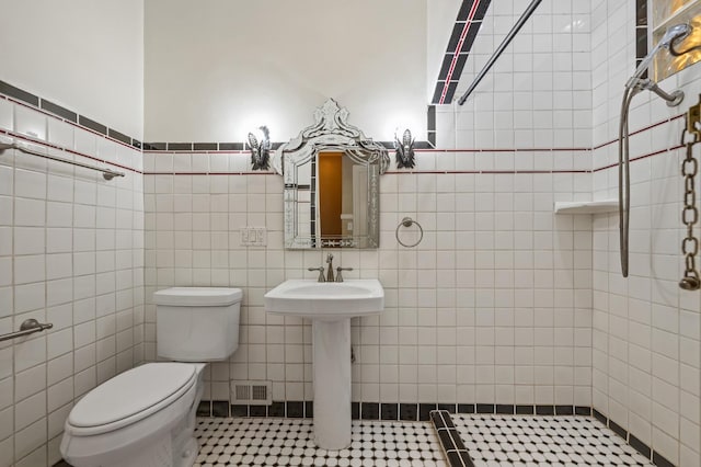 bathroom with toilet, tile patterned floors, tile walls, and sink