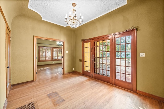 entryway featuring french doors, a textured ceiling, light wood-type flooring, and a notable chandelier