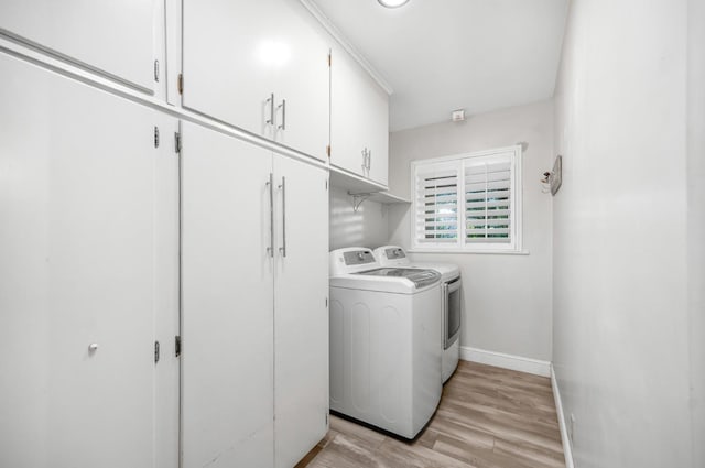 clothes washing area featuring cabinets, washing machine and dryer, and light wood-type flooring