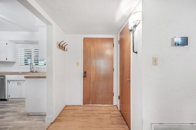 hall featuring sink, light wood-type flooring, and a textured ceiling