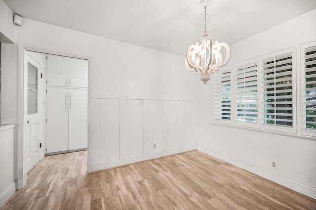 spare room with a notable chandelier and light wood-type flooring