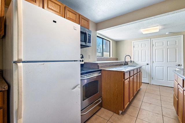 kitchen with sink, a textured ceiling, light tile patterned floors, and appliances with stainless steel finishes