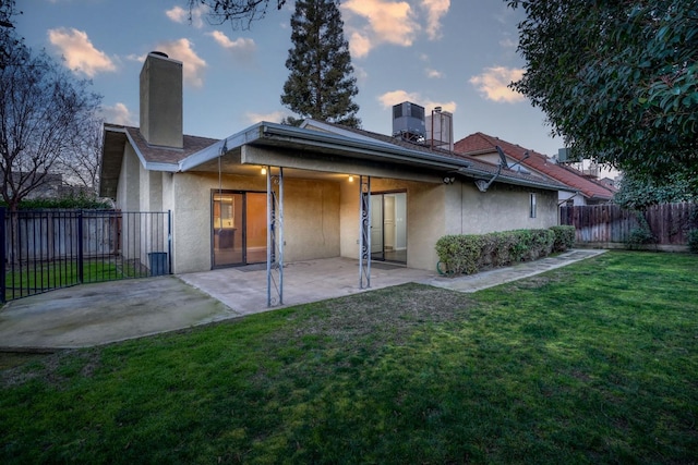 back house at dusk with a patio, central AC, and a yard