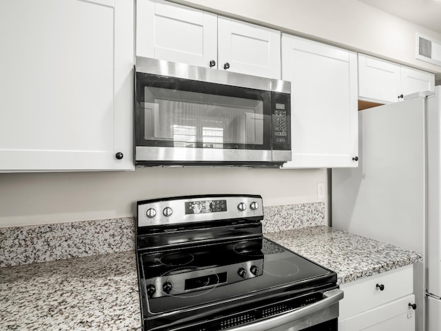 kitchen featuring visible vents, appliances with stainless steel finishes, white cabinets, and light stone counters