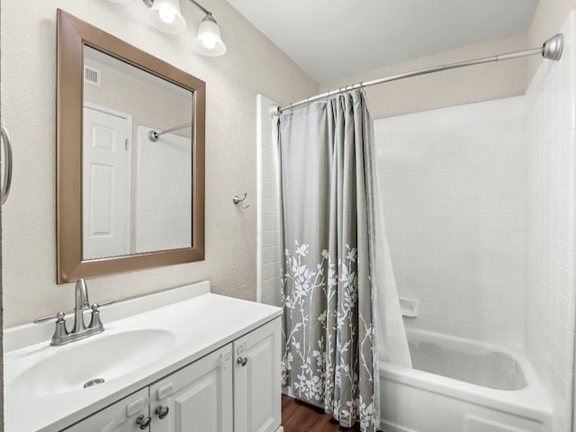 bathroom with a textured wall, shower / tub combo, wood finished floors, vanity, and visible vents