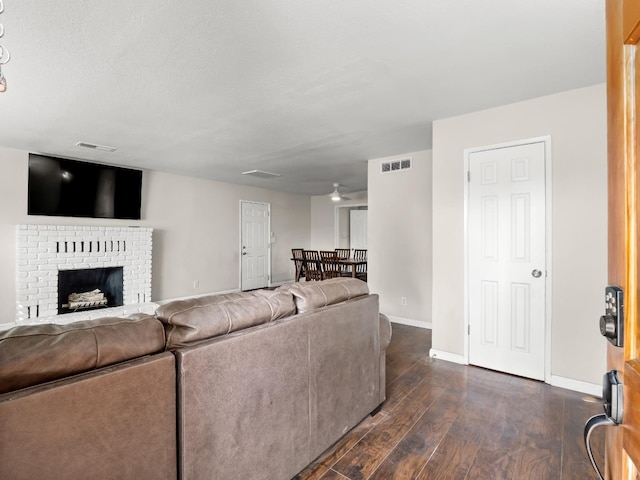 living area with a brick fireplace, baseboards, visible vents, and dark wood-style flooring