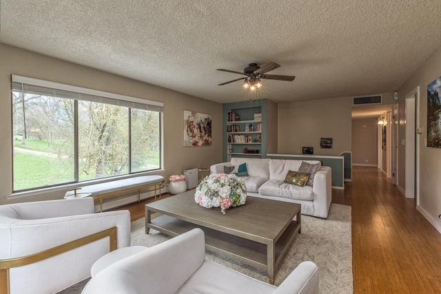 living room featuring baseboard heating, a textured ceiling, ceiling fan, and wood-type flooring