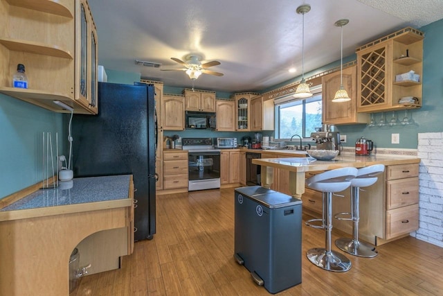 kitchen with black appliances, light hardwood / wood-style floors, kitchen peninsula, a kitchen bar, and decorative light fixtures