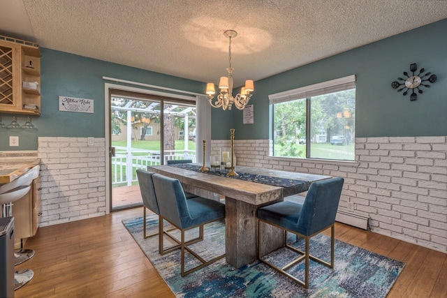 dining room featuring a textured ceiling, dark wood-type flooring, an inviting chandelier, and brick wall