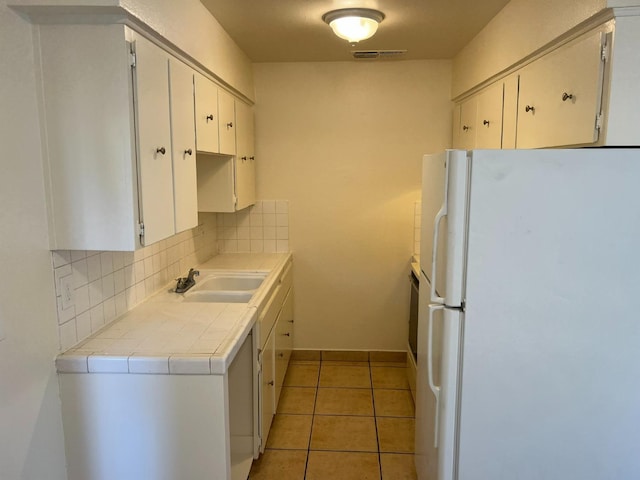 kitchen featuring tile counters, decorative backsplash, white cabinetry, white refrigerator, and sink