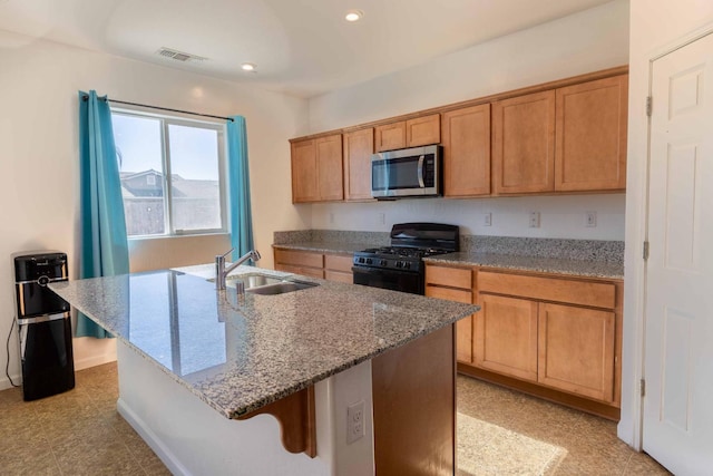 kitchen with sink, black gas stove, an island with sink, light stone countertops, and a breakfast bar