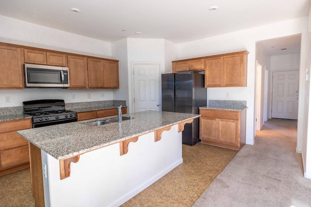 kitchen featuring light stone counters, an island with sink, a breakfast bar, black appliances, and sink