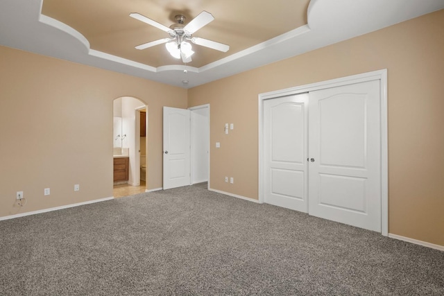 unfurnished bedroom featuring carpet, ceiling fan, a closet, ensuite bath, and a tray ceiling