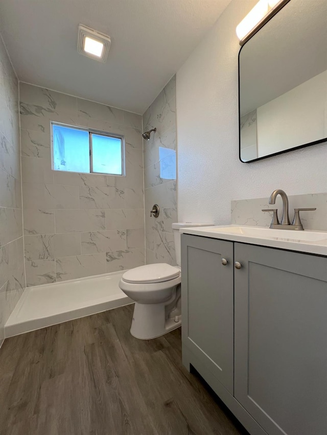 bathroom with toilet, a tile shower, vanity, and hardwood / wood-style floors