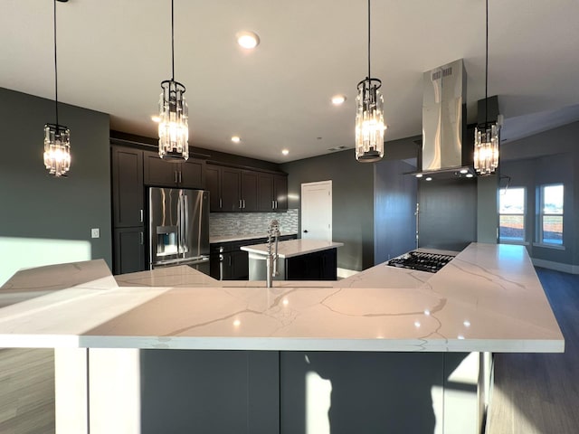 kitchen featuring a large island with sink, decorative backsplash, hanging light fixtures, stainless steel appliances, and island range hood