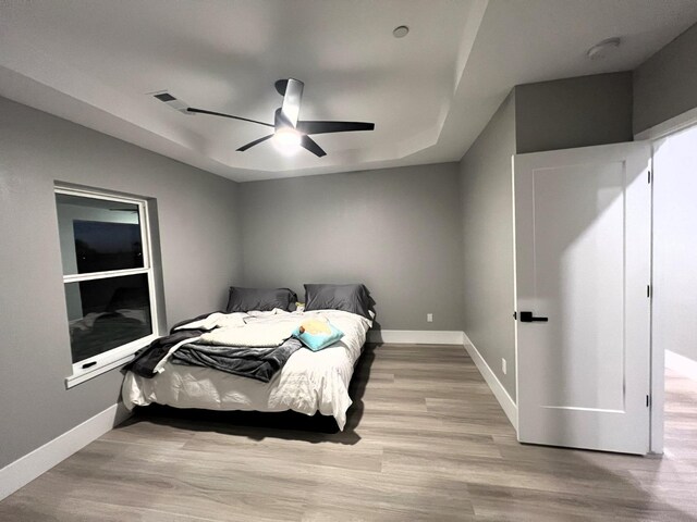 bedroom with light wood-type flooring, ceiling fan, and a raised ceiling