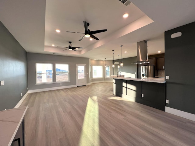 kitchen with ceiling fan, stainless steel refrigerator with ice dispenser, island exhaust hood, a tray ceiling, and hanging light fixtures