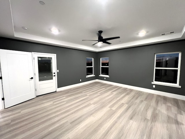 interior space featuring a raised ceiling, ceiling fan, and light hardwood / wood-style flooring