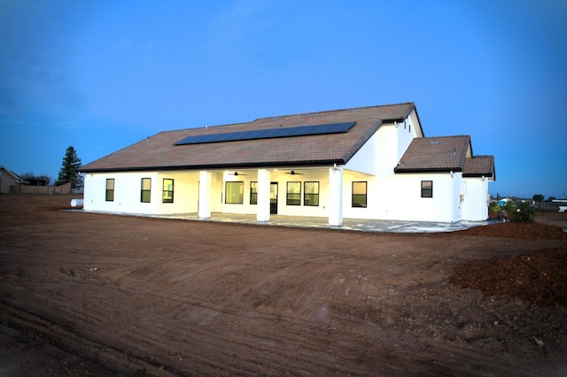 back house at dusk with ceiling fan, solar panels, and a patio