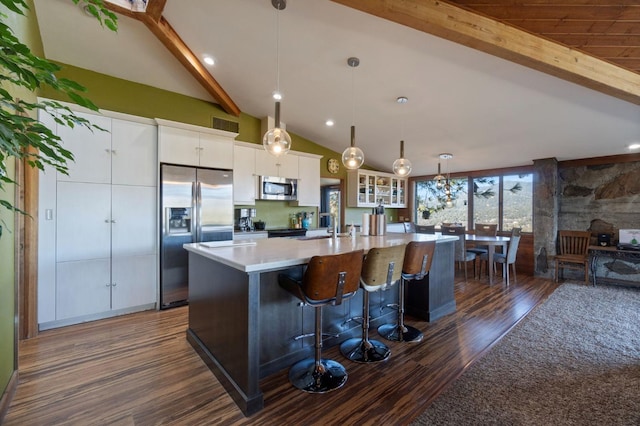 kitchen with appliances with stainless steel finishes, a large island with sink, dark hardwood / wood-style flooring, white cabinetry, and decorative light fixtures