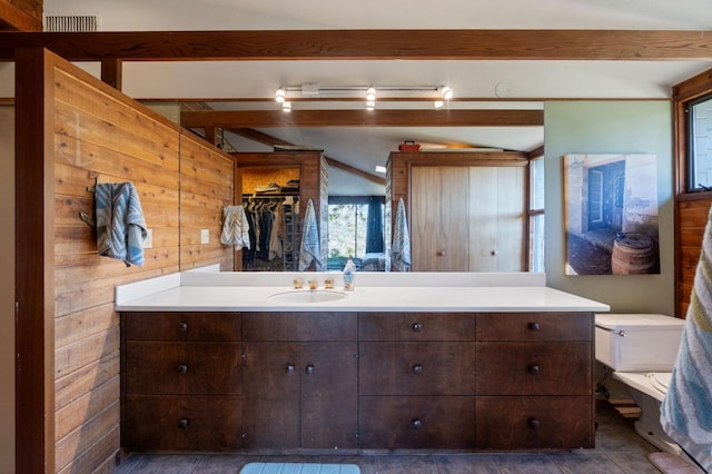 bathroom featuring beam ceiling, wooden walls, vanity, and toilet