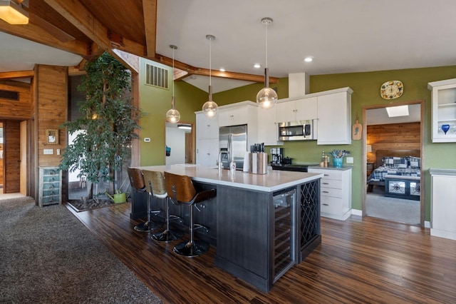 kitchen featuring appliances with stainless steel finishes, hanging light fixtures, white cabinetry, and a kitchen island with sink