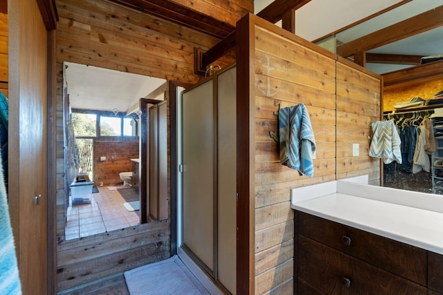 bathroom featuring toilet, tile patterned flooring, wooden walls, an enclosed shower, and vanity