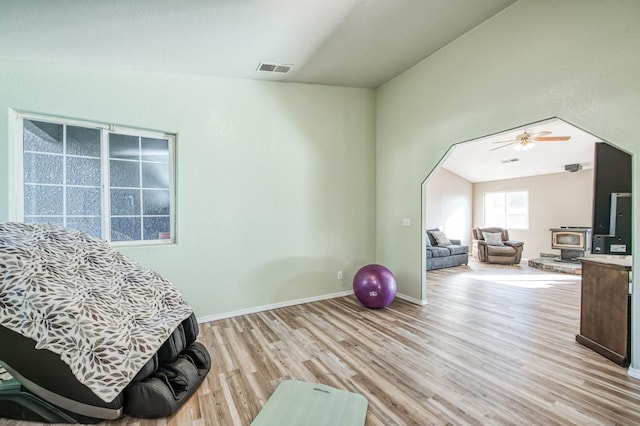 interior space with ceiling fan, light wood-type flooring, vaulted ceiling, and a wood stove