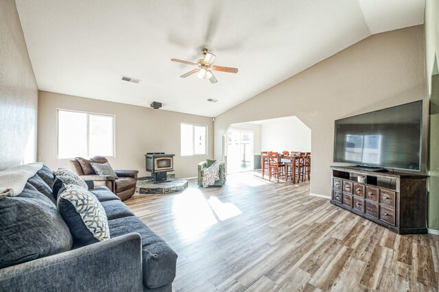 living room with vaulted ceiling, light wood-type flooring, ceiling fan, and a wood stove