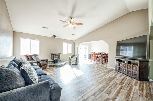 living room with visible vents, lofted ceiling, ceiling fan, a wood stove, and light wood-style floors