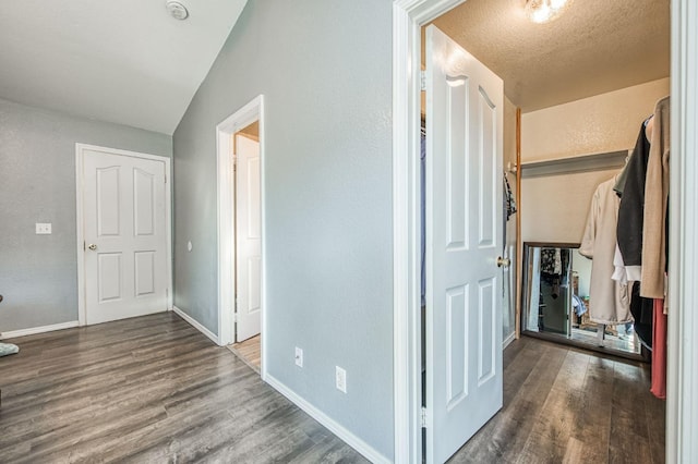 corridor with a textured ceiling, a textured wall, wood finished floors, and baseboards