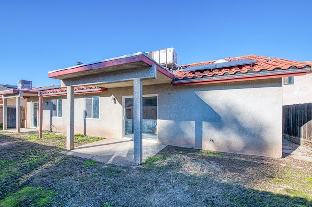 back of house featuring a tile roof, a patio, stucco siding, roof mounted solar panels, and fence