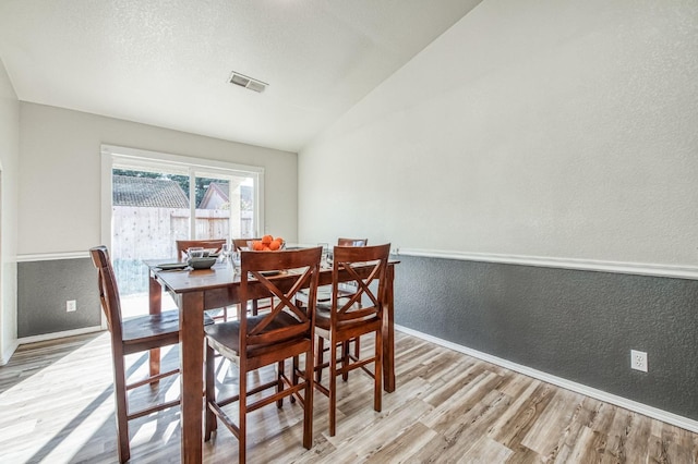 dining space with a textured wall, visible vents, vaulted ceiling, and light wood finished floors